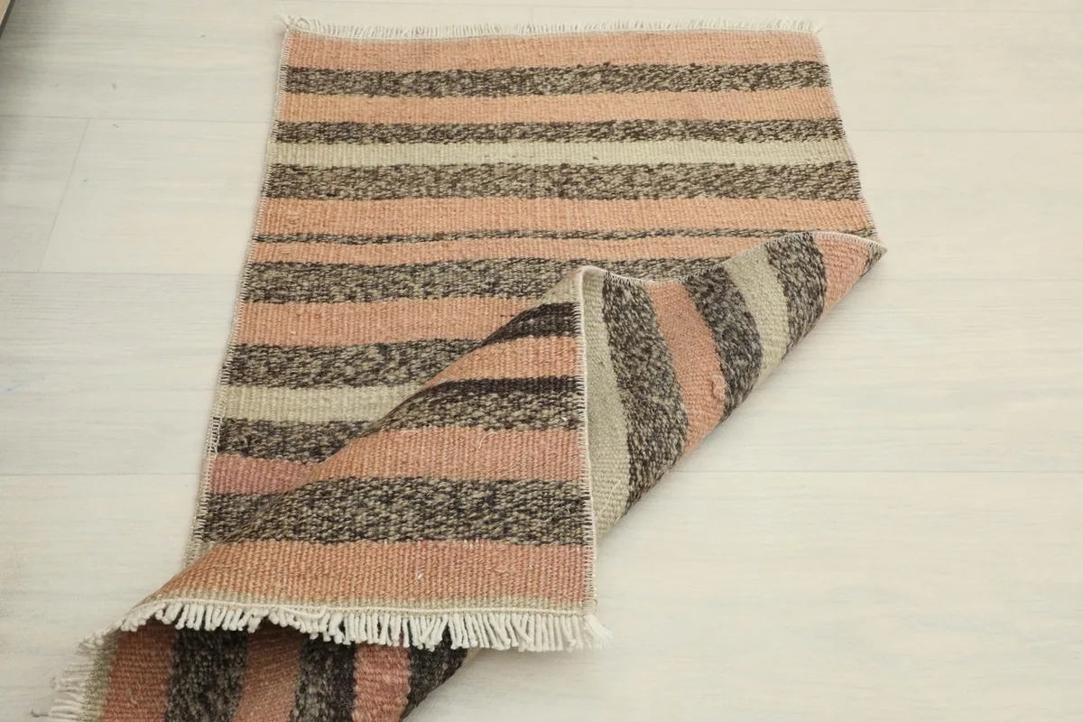 Partially folded rug on a light background, emphasizing its compact size and striped design.