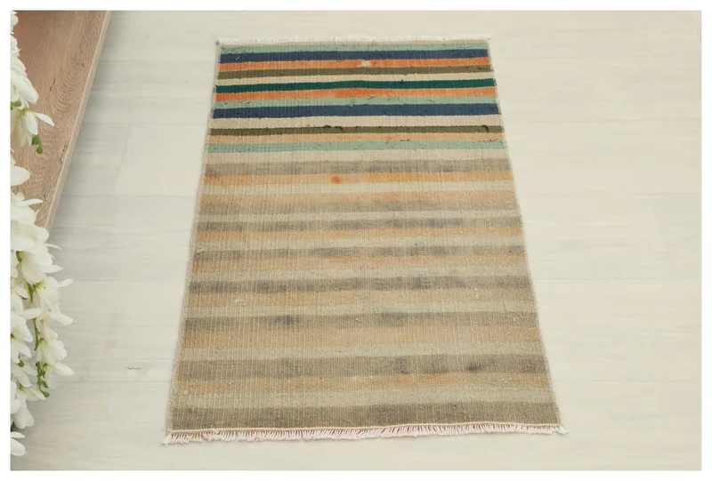 Full overhead view of a 1'6" x 2'7" muted multicolor striped vintage Anatolian wool doormat on a white background.