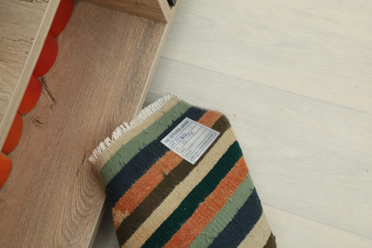 The doormat rolled up with its label, placed next to a wooden shelf, showing its compact size.