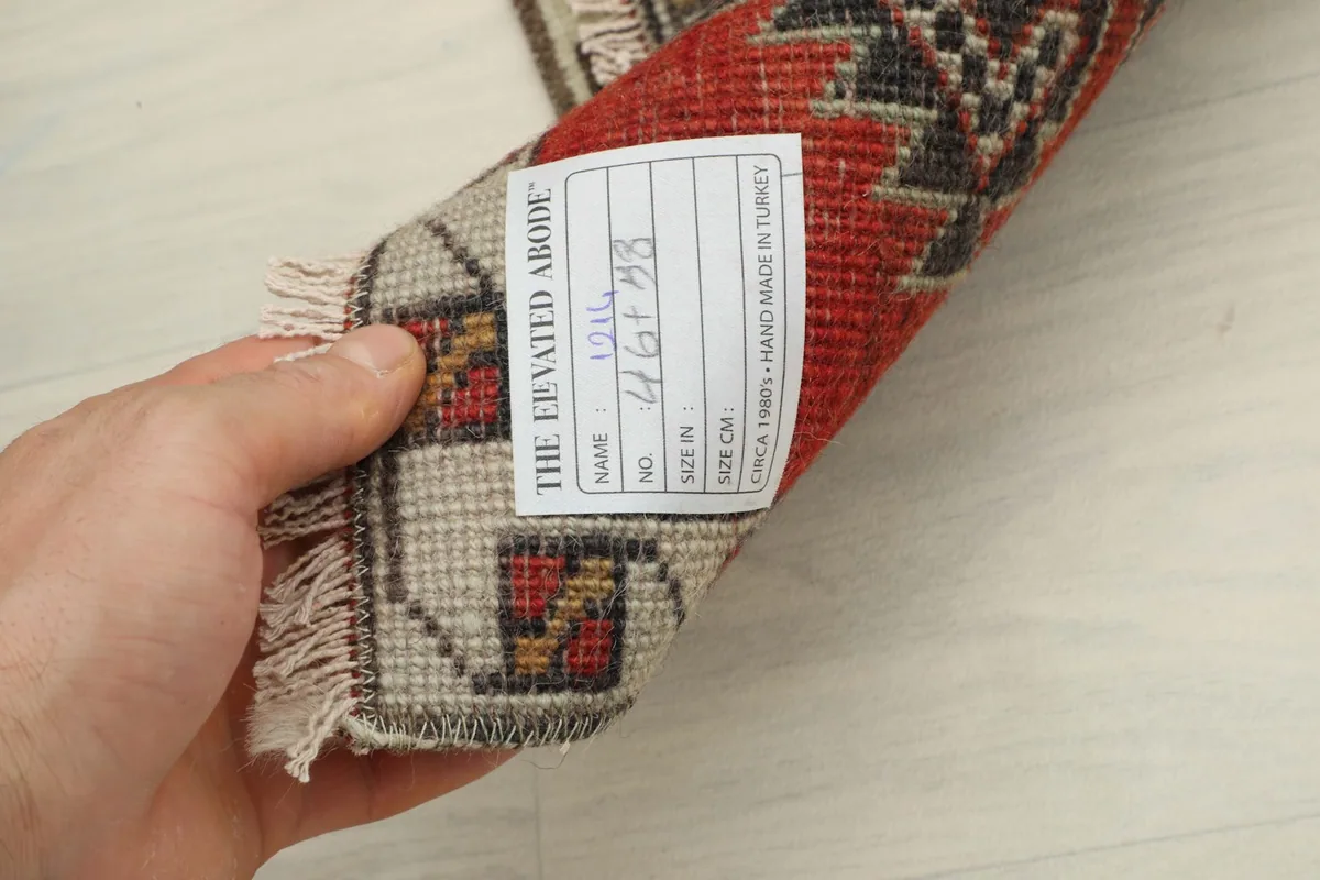 Hand holding the rolled rug, revealing the back and a tag with size and origin details