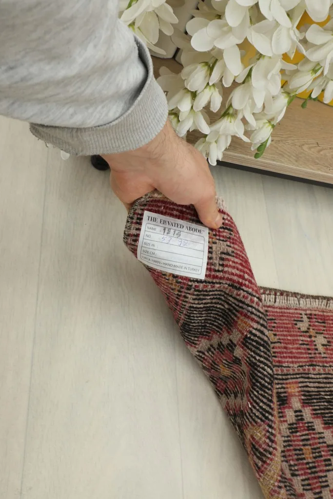 Hand holding the rug to show the label and the back of the vintage doormat