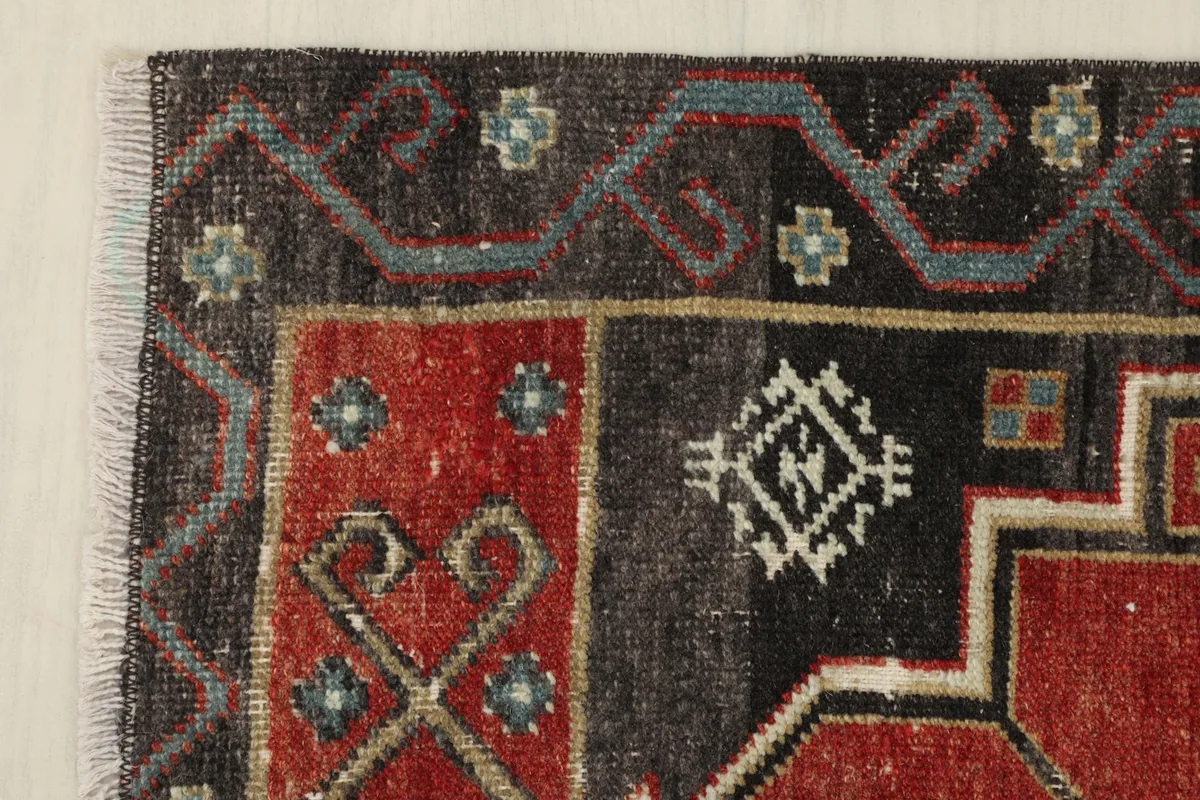 Corner detail of the rug, displaying the intersection of the rust field and charcoal border with blue elements.