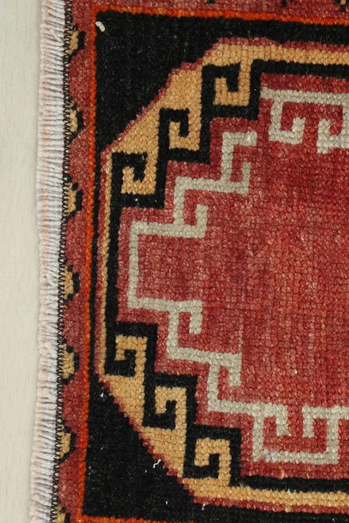 Close-up detail of the top left corner of the rug, showing red, black, and tan geometric patterns.