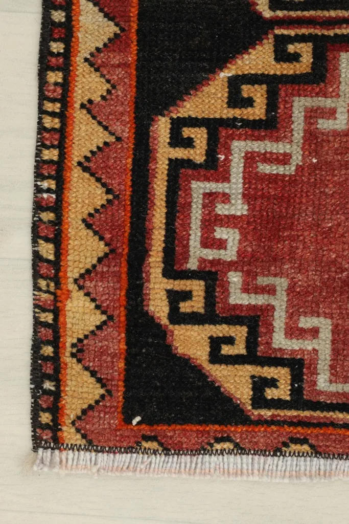 Close-up of the bottom left corner, showing the red field, black details, and tan border.