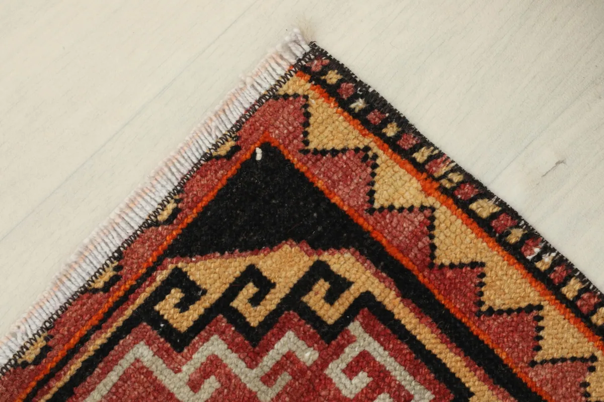 Detailed view of the rug's border and corner, featuring zig-zag patterns in tan and red.