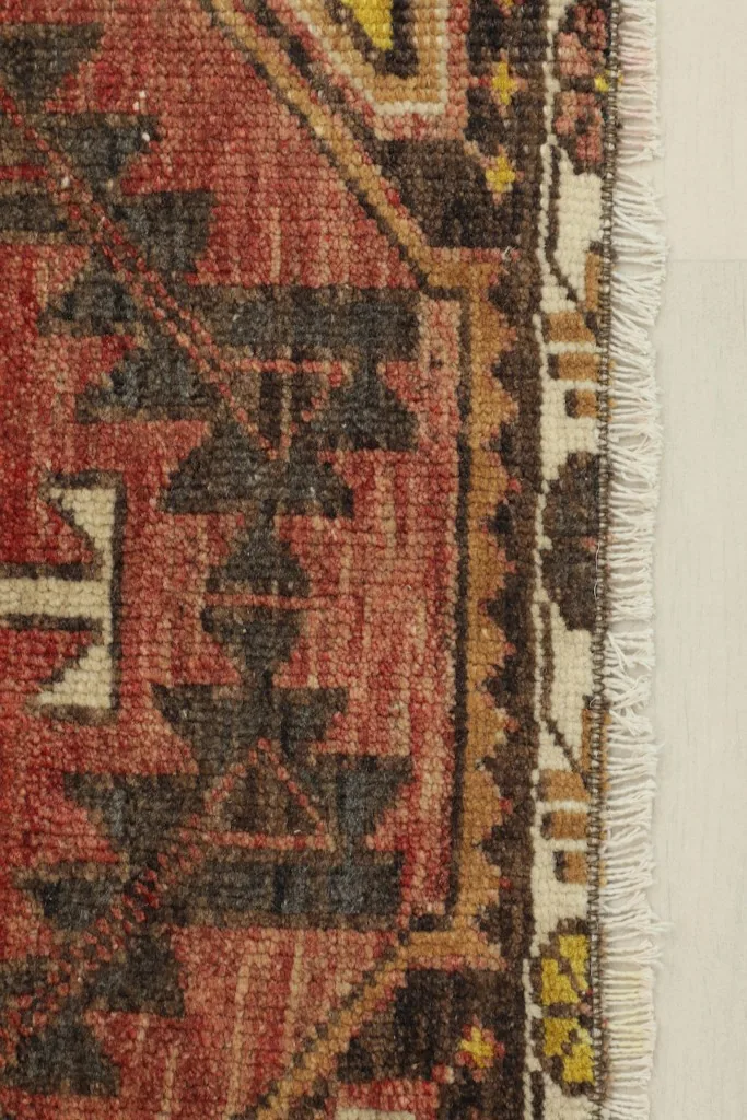 Close-up detail of the rug's red field, brown geometric motifs, and the fringe along the edge.