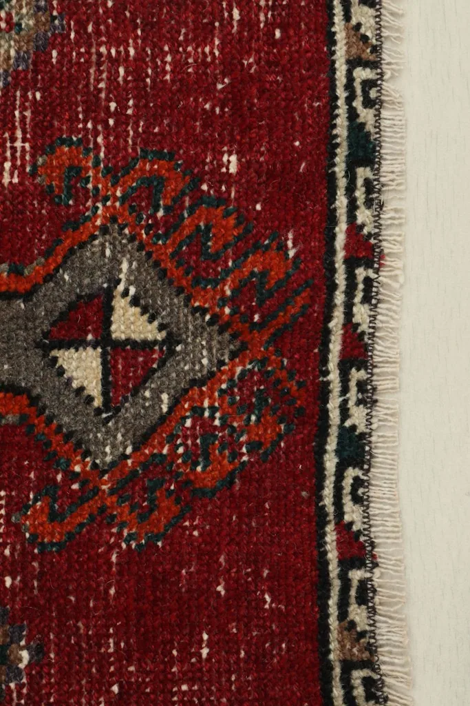 Close-up detail of the red field and a corner of the gray geometric motif on the vintage rug.