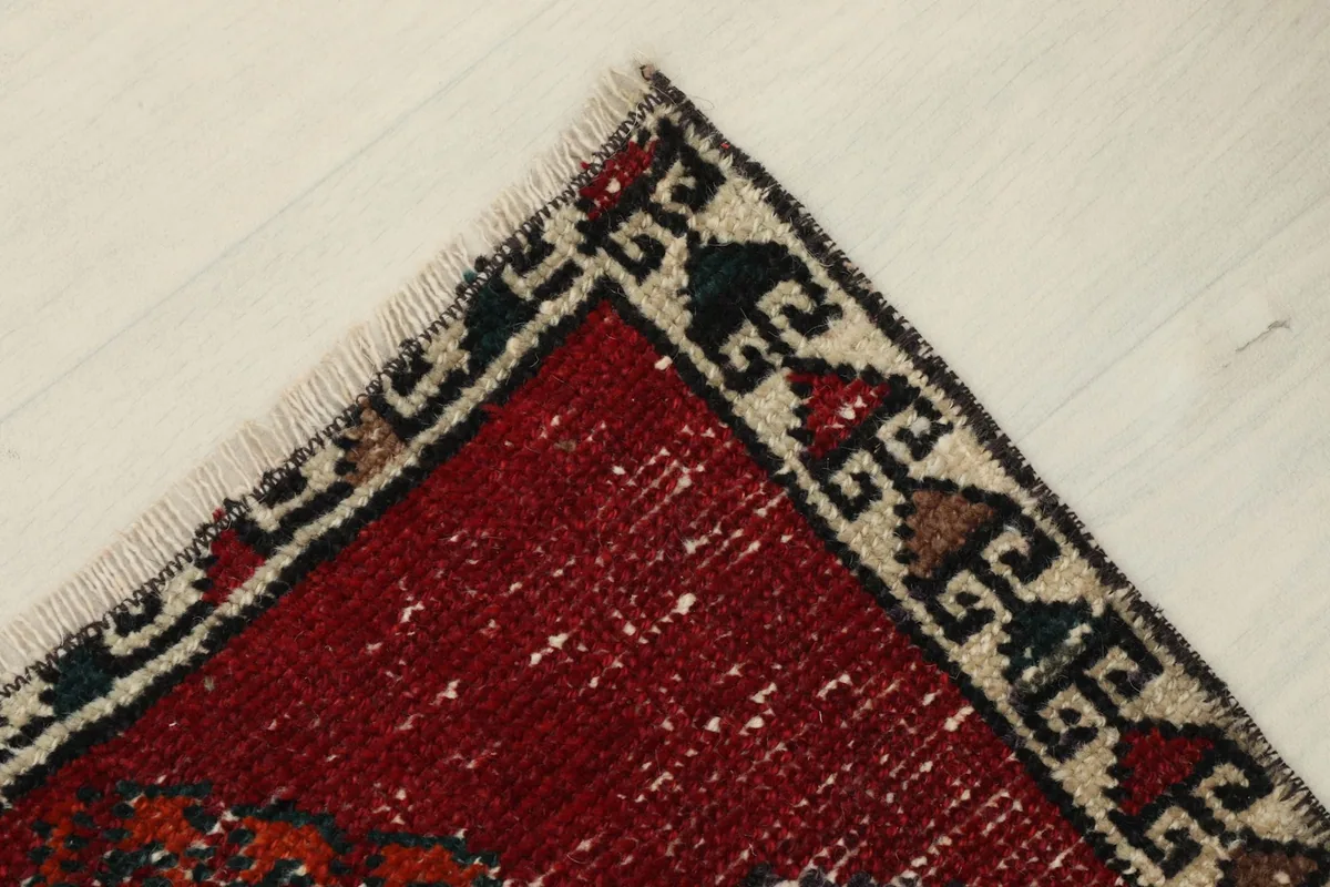 Close-up of a corner of the rug, showing the beige and black patterned border and red field.