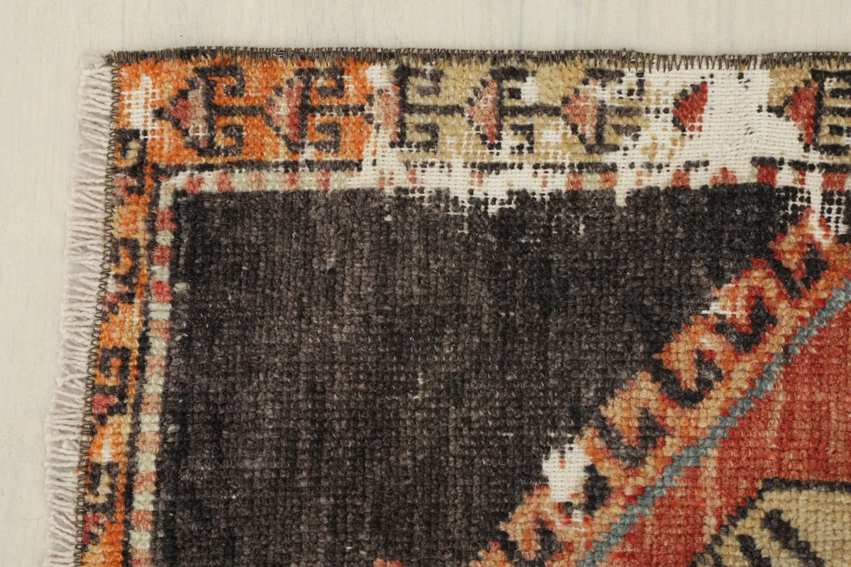Corner detail of the rug, highlighting the charcoal field and the decorative border with orange and beige elements.