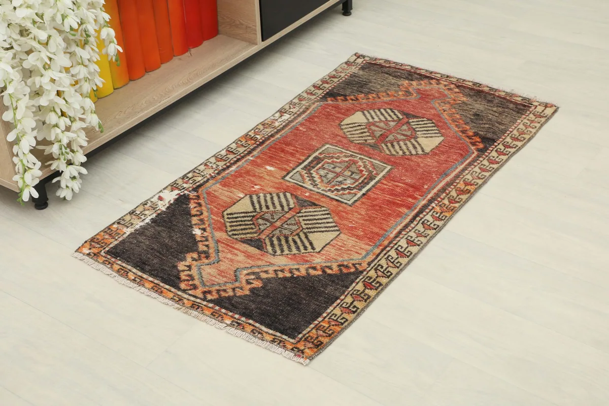 Overhead angled view of the small rust and charcoal rug on a light floor, next to a shelf.