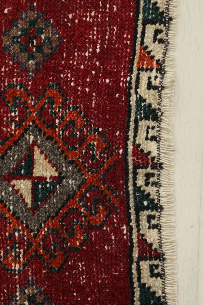 Close-up detail of the rug's red field, showing the texture, subtle wear, and a portion of the beige and navy border.