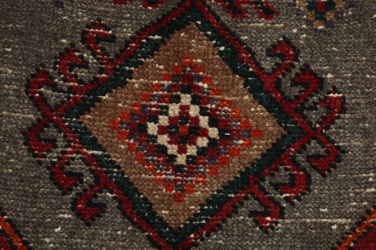 Zoomed-in detail of a complex diamond motif within the gray central design, featuring red, navy, and beige threads.