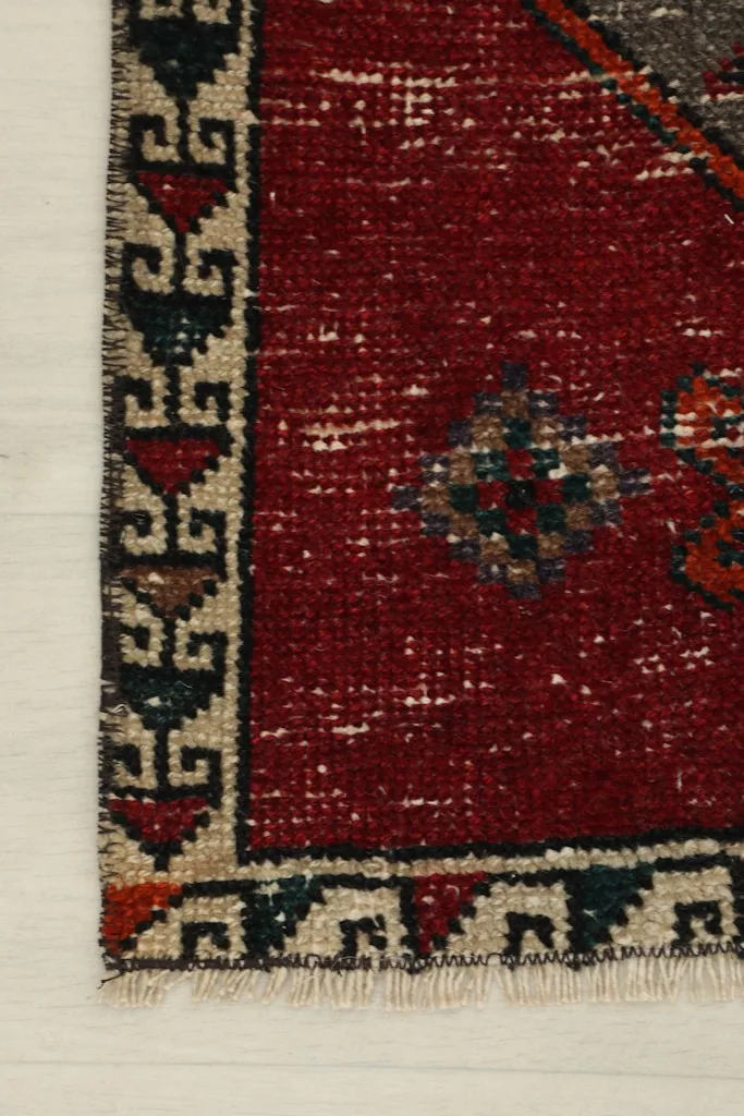Close-up of the rug's border design, showing the beige and navy geometric patterns against the distressed red field.