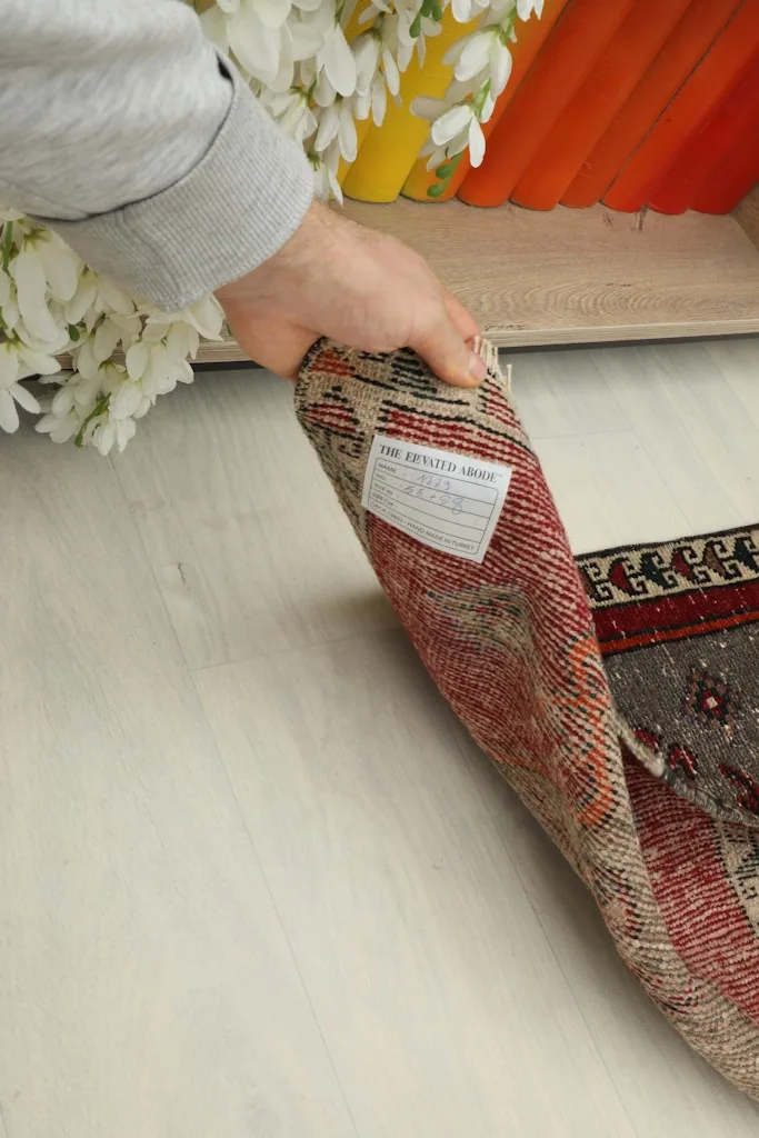 A hand holding the folded rug, displaying the back of the rug and a label, indicating its hand-knotted construction.