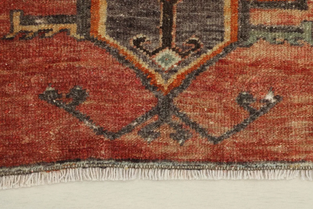 Close-up detail of the hand-knotted pile and tribal motifs in rust, charcoal, and orange colors.