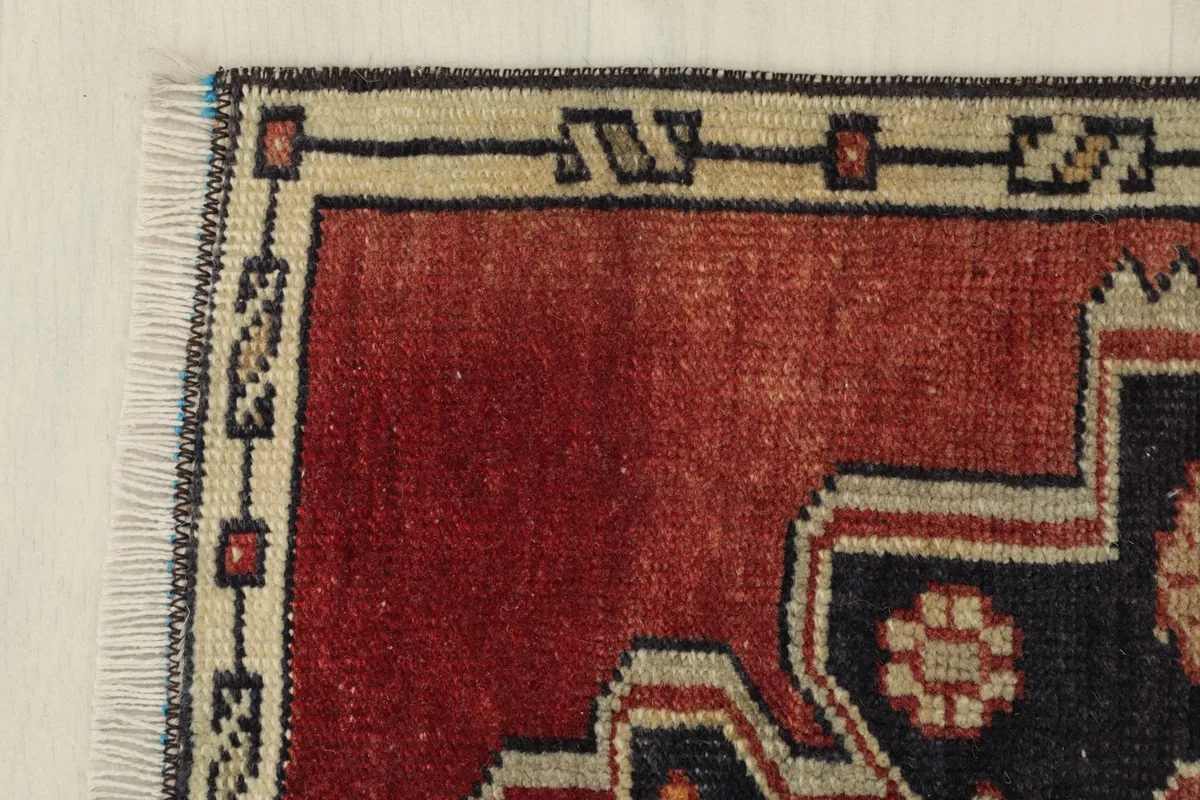 Corner detail of the rug, showing the ivory border with geometric motifs against the red field.