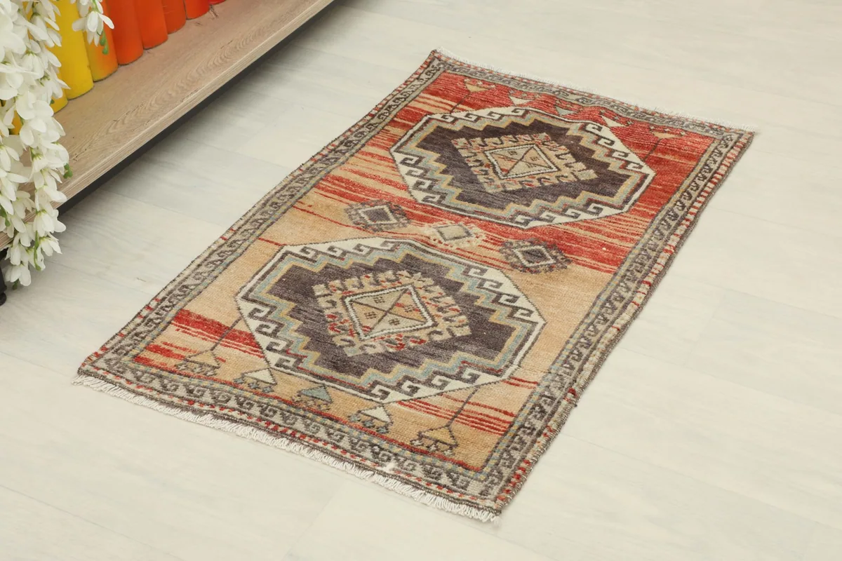 Angled view of the small hand-knotted rug, showing its geometric medallions and red stripes