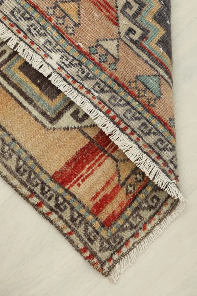 Rug corner folded back to reveal the back of the rug and the cotton foundation