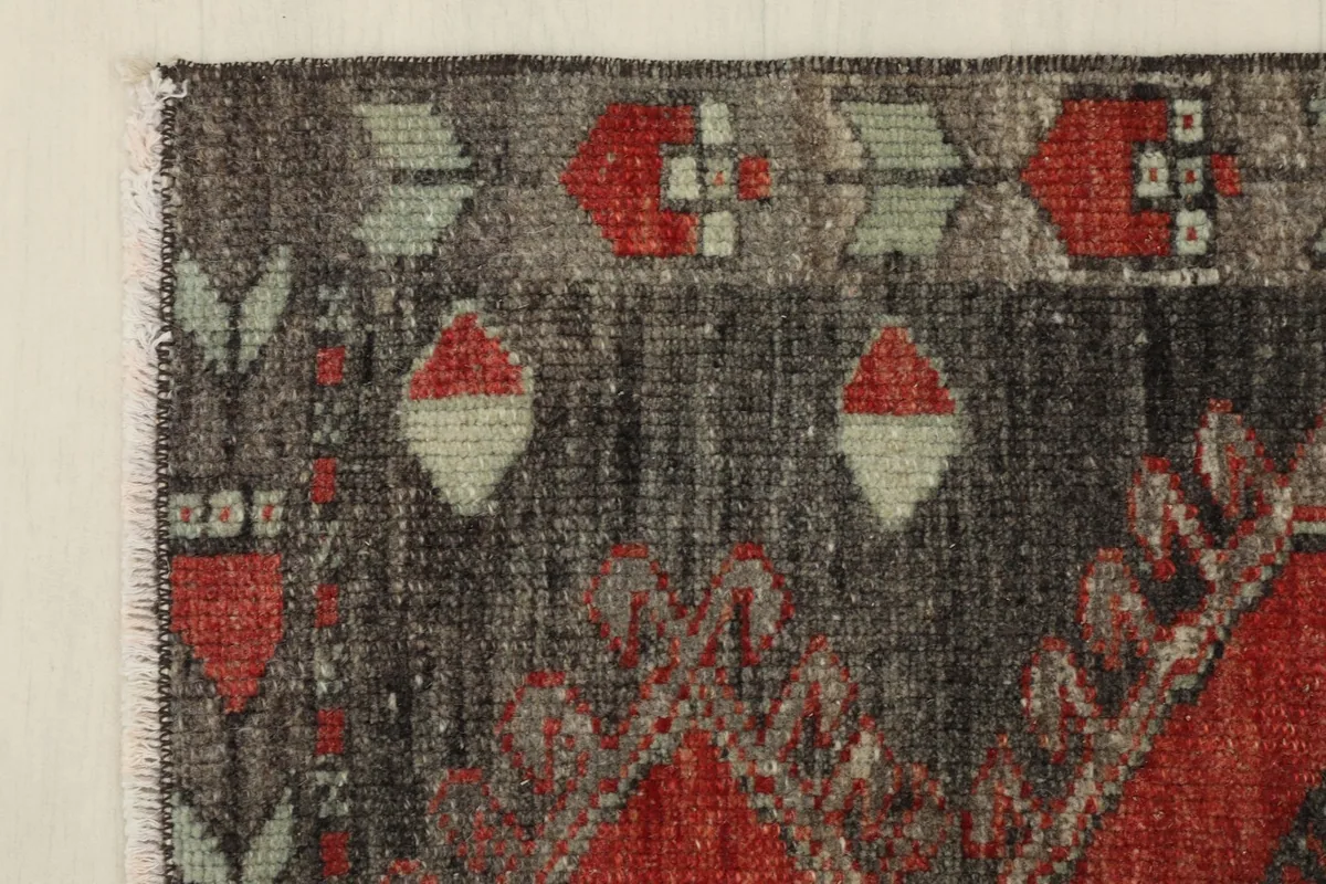 Close-up of the rug's border with red and green tribal patterns on a charcoal field