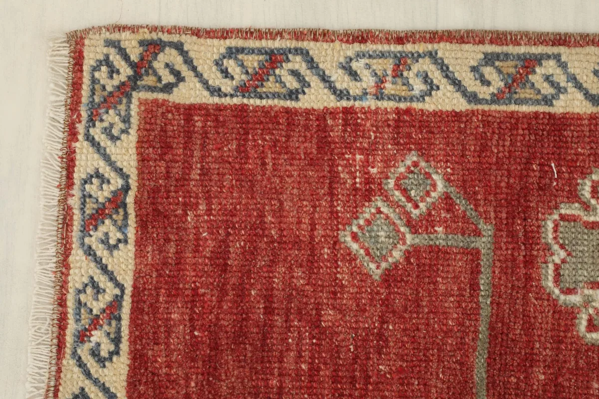 Corner detail of the rug, highlighting the beige border with blue and red geometric designs.