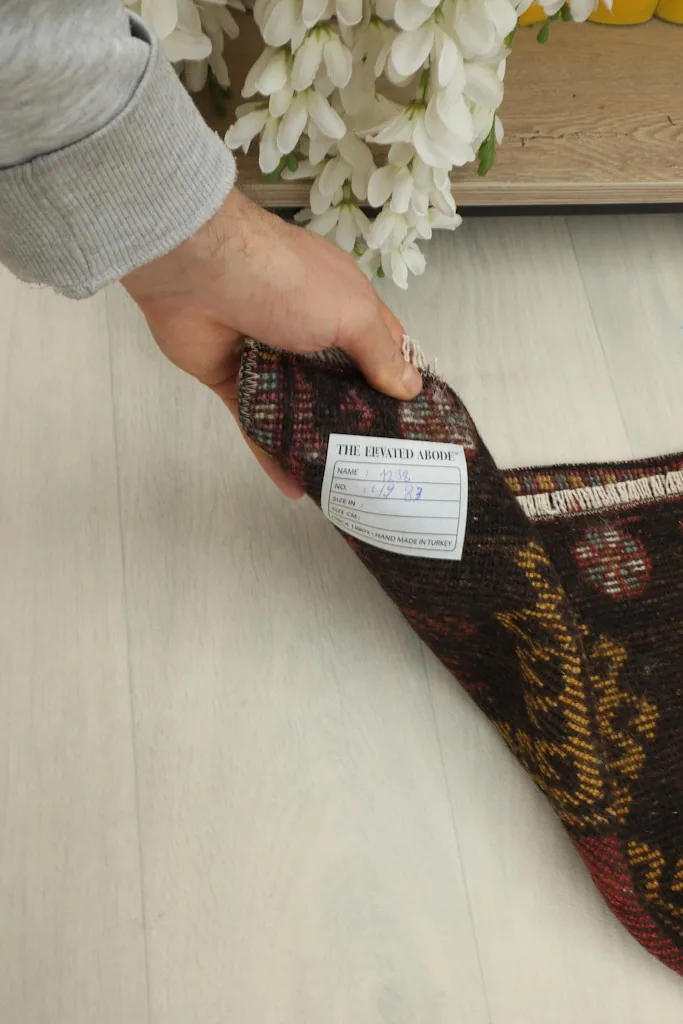 A hand holding the rug, revealing the back of the rug and the woven label.
