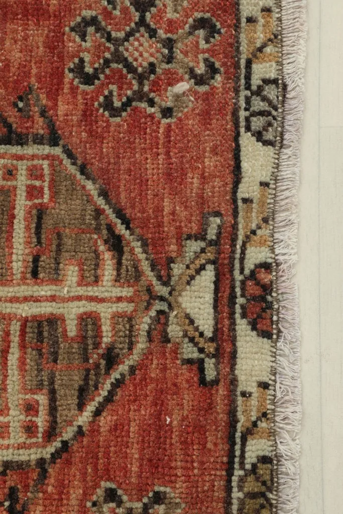 Close-up detail of the rust field, geometric motif, and beige border of the rug
