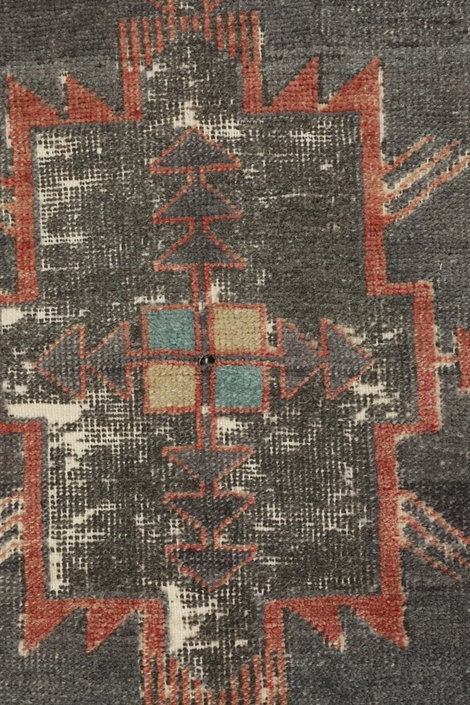 Close-up of the central motif within the charcoal medallion, highlighting blue and tan accents.