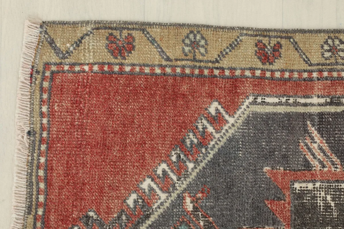 Corner detail showing the red field, charcoal pattern, and the tan border with small floral motifs.