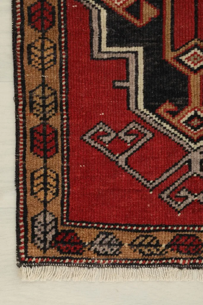 Detail of the rug's corner, showing the tan border with red and gray elements and fringe.