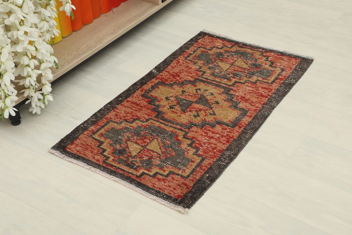 Slightly angled overhead view of the small red and gold tribal rug on a light floor