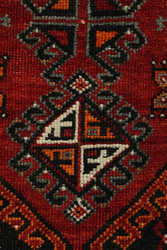 Close-up of a central geometric motif with red, black, orange, and ivory wool knots