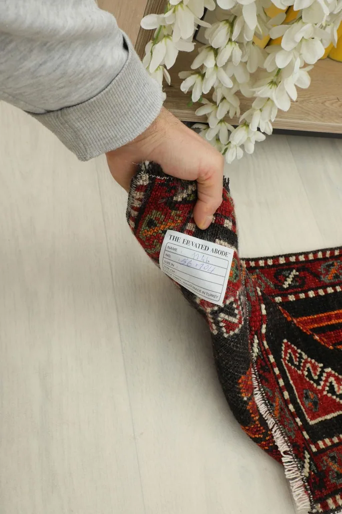 A hand holding the rug, revealing the back of the hand-knotted cotton foundation