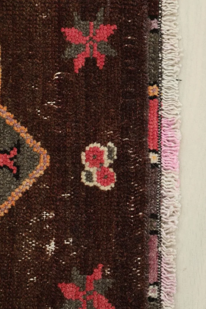 Close-up of the rug's border and fringe, highlighting the rose and gray tones and wool texture.