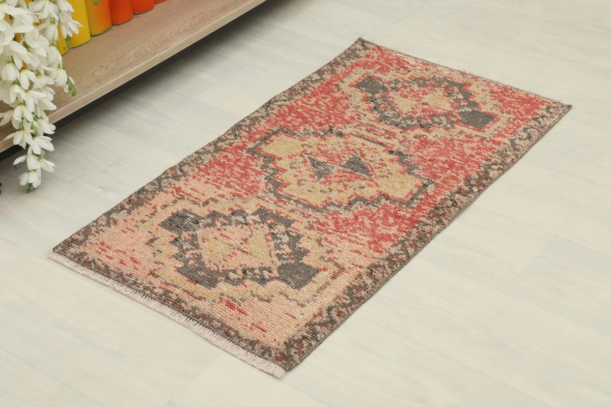Angled view of the vintage doormat rug, showing its rectangular shape and faded rose and tan colors.