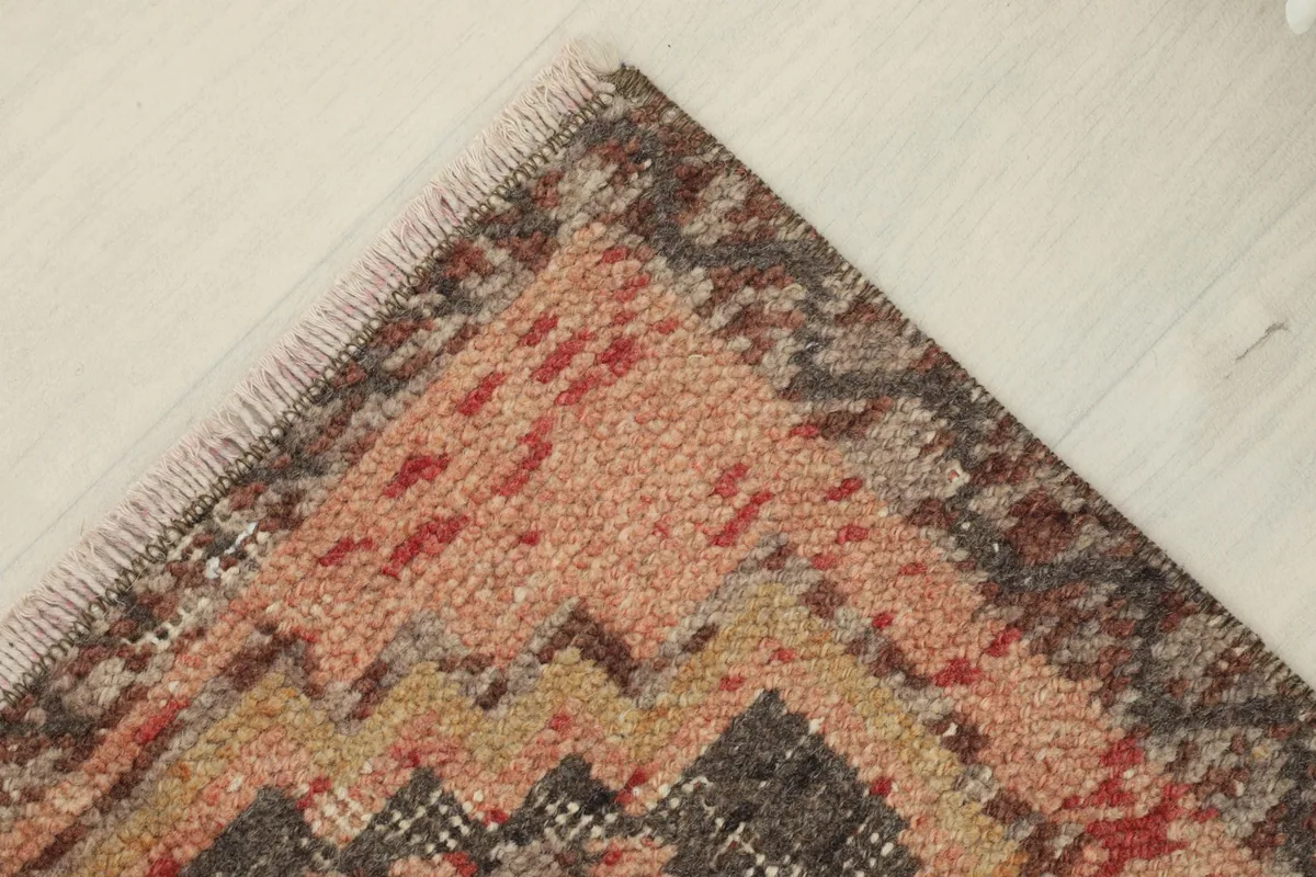 Corner view of the rug, illustrating the defined edges and the blend of rose, tan, and charcoal fibers.