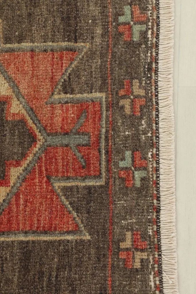 Close-up detail of the rug's edge, highlighting the red and gray geometric patterns and the short fringe.