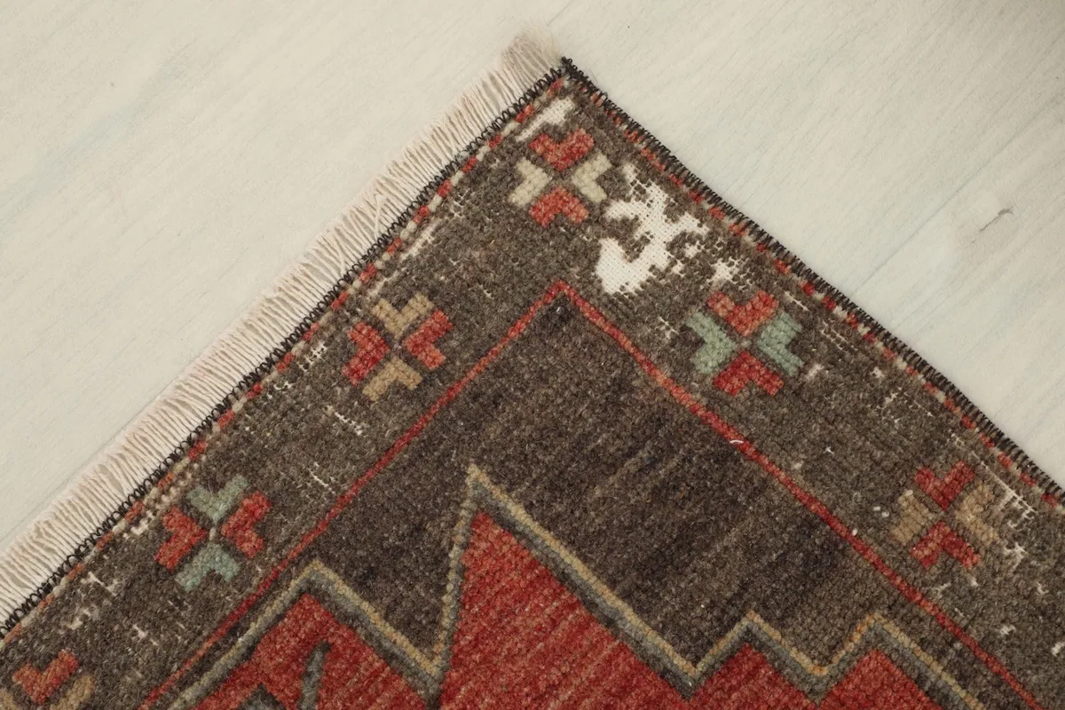Corner detail of the rug, showing the distressed brown field and intricate tribal motifs with tan and green accents.