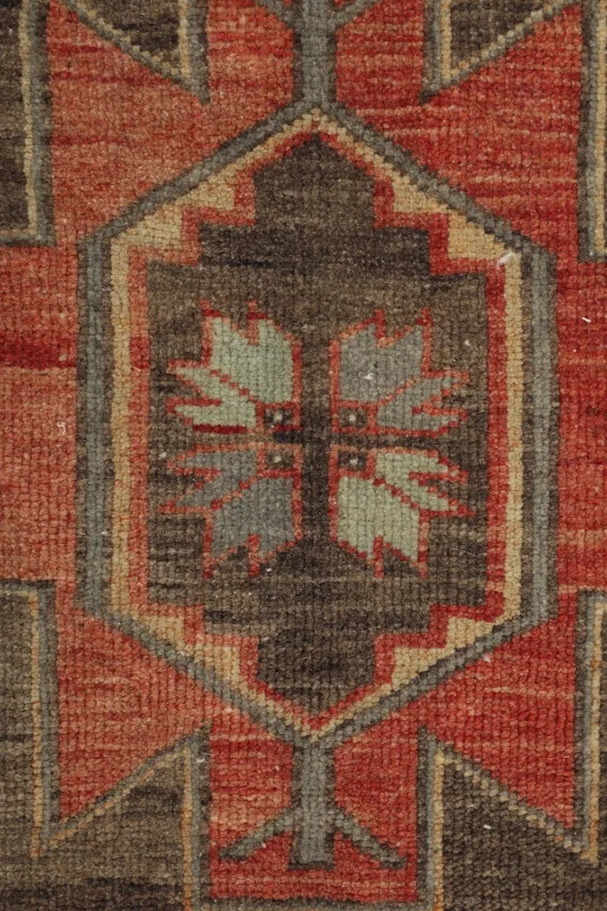 Close-up of a central geometric motif with leaf-like elements in gray, tan, and brown against an orange background.