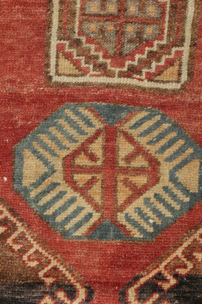 Detailed view of an individual geometric motif in blue, tan, and red on the rug's red field.