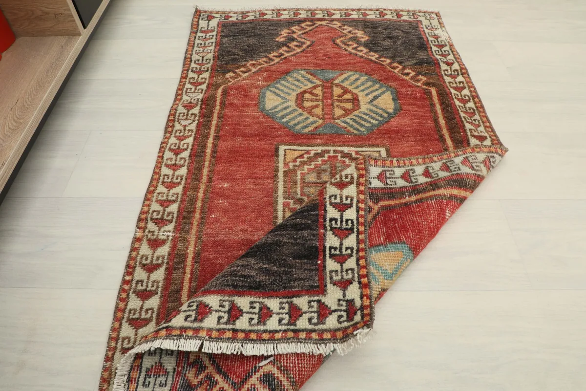 The red tribal rug partially folded, demonstrating its flexibility and texture.