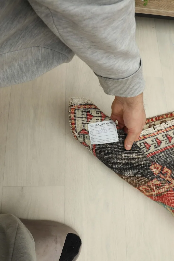 A hand holding the rug, showing its size and the tag on the back.
