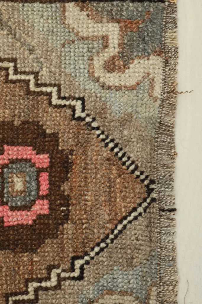 Close-up detail of the rug's edge, showing the hand-knotted texture and a section of the blue and brown pattern.