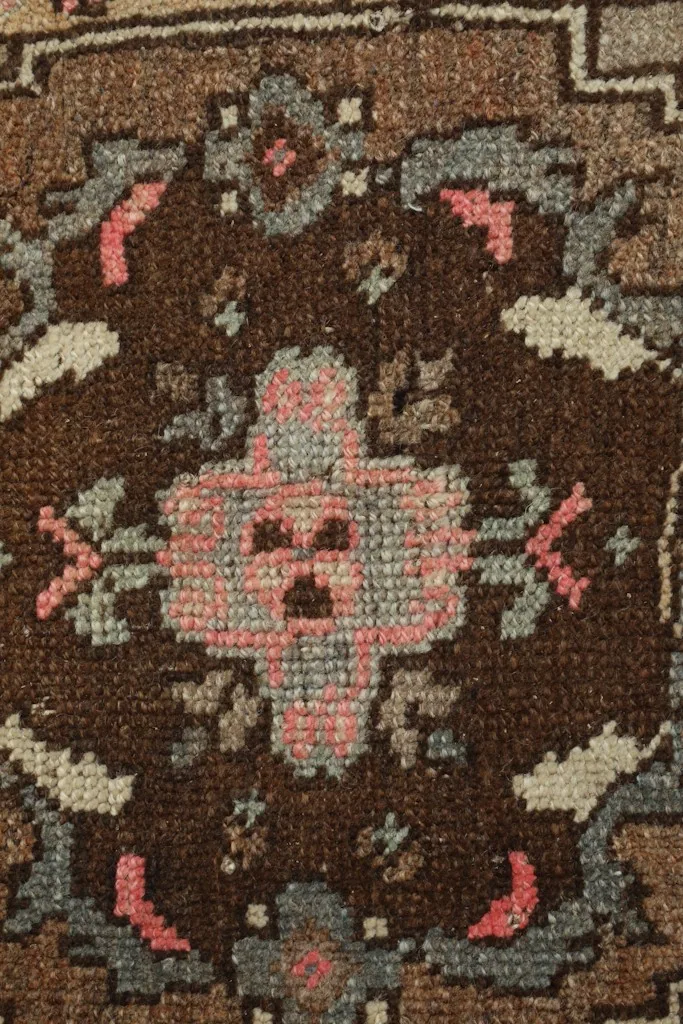 Tight detail shot of the rug's central pink and blue floral motif against the dark brown field.