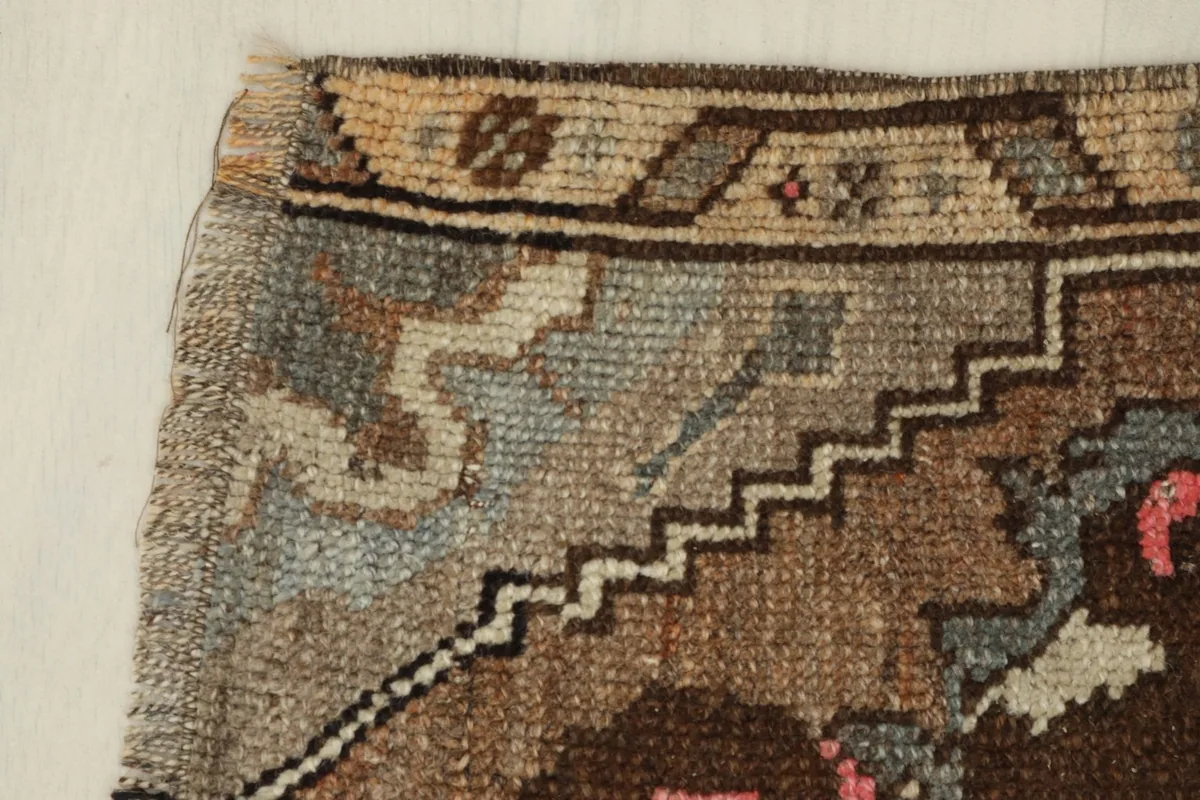 Close-up of the rug's border, highlighting the beige and brown tones and geometric step patterns.