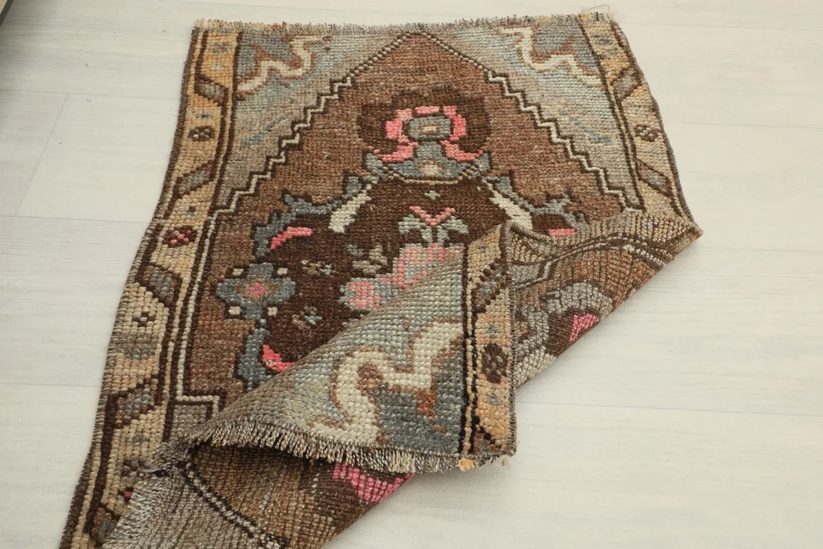 The rug partially folded, displaying the back and front textures, with the brown and pink patterns visible.