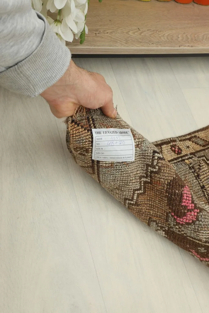 A hand holding the rolled rug, showing the product label and the density of the vintage wool pile.