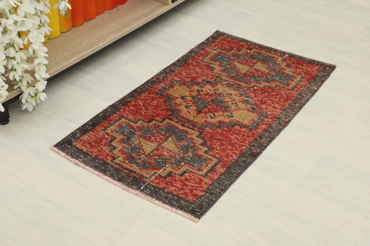 Angled view of the vintage doormat showcasing its red, brown, and tan geometric patterns.