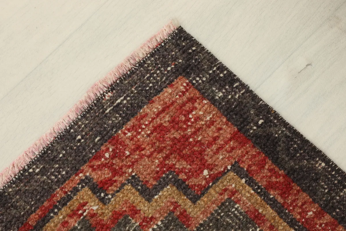 Corner view of the rug, showing the fringe and the blend of red, brown, and tan colors.