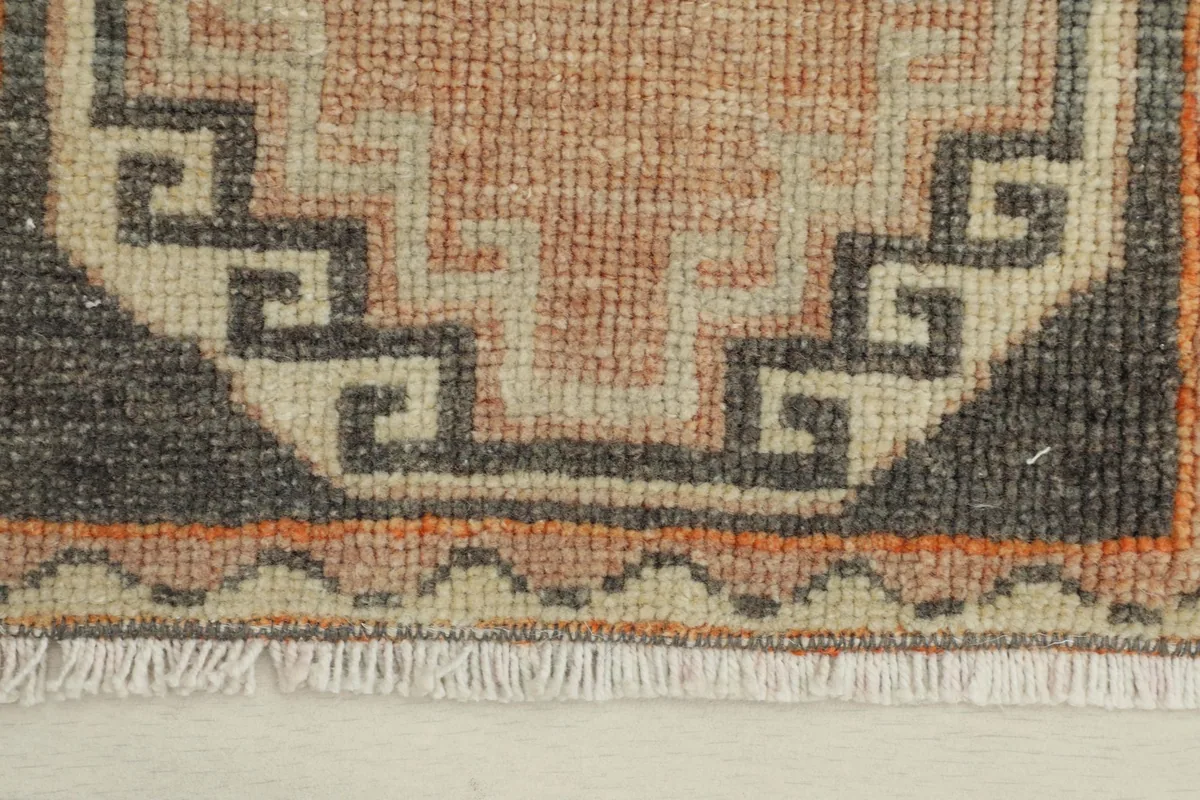 Close-up detail of the hand-knotted wool pile and geometric motifs in rose, charcoal, and beige