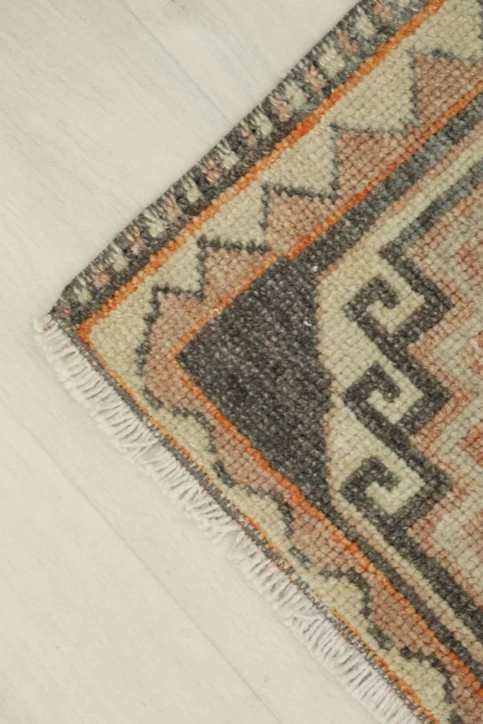 Corner detail of the rug, showing the orange and beige border design and fringed edge